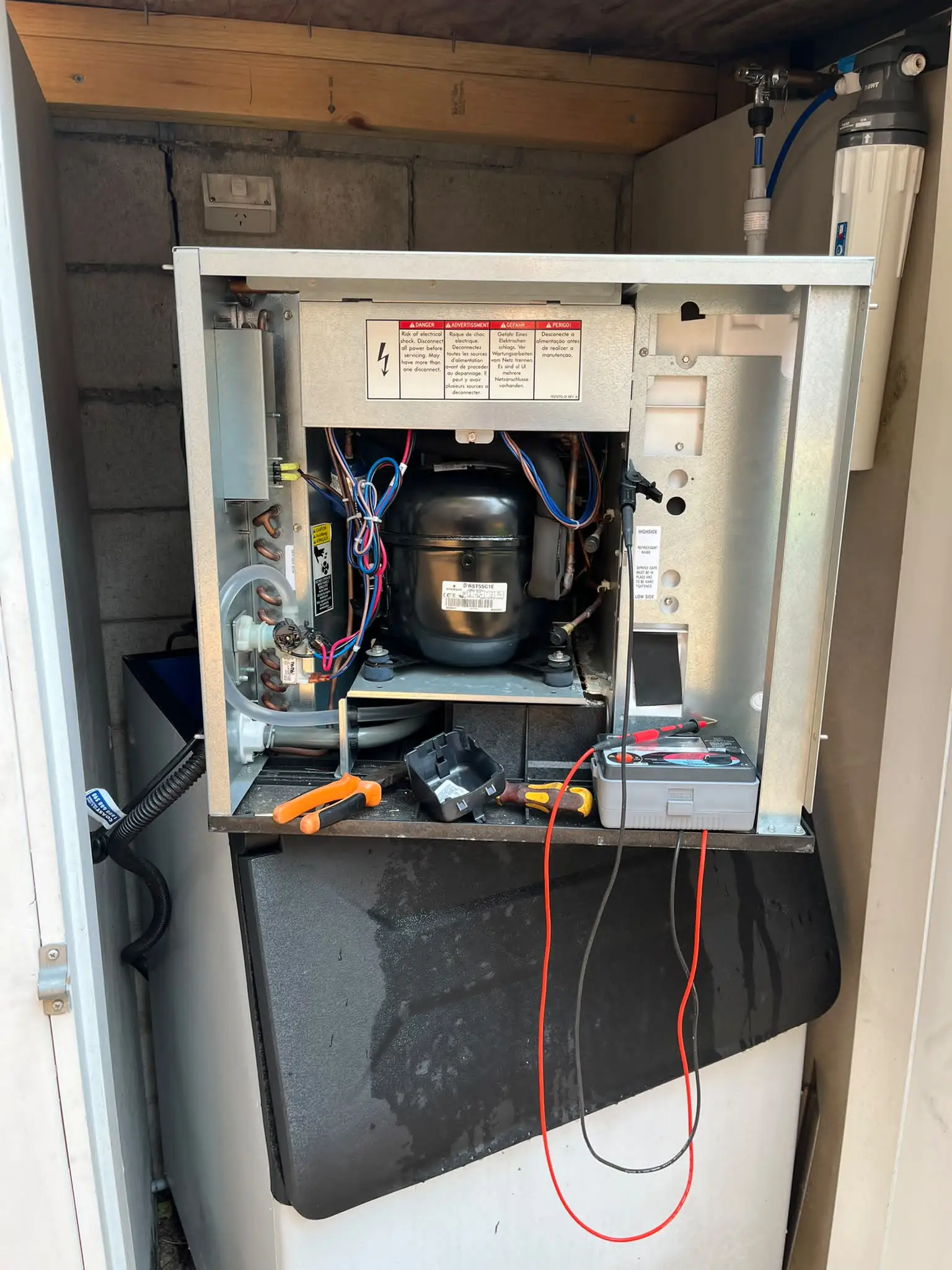 Commercial ice machine opened for diagnosis with its compressor, wiring and testing tools visible
