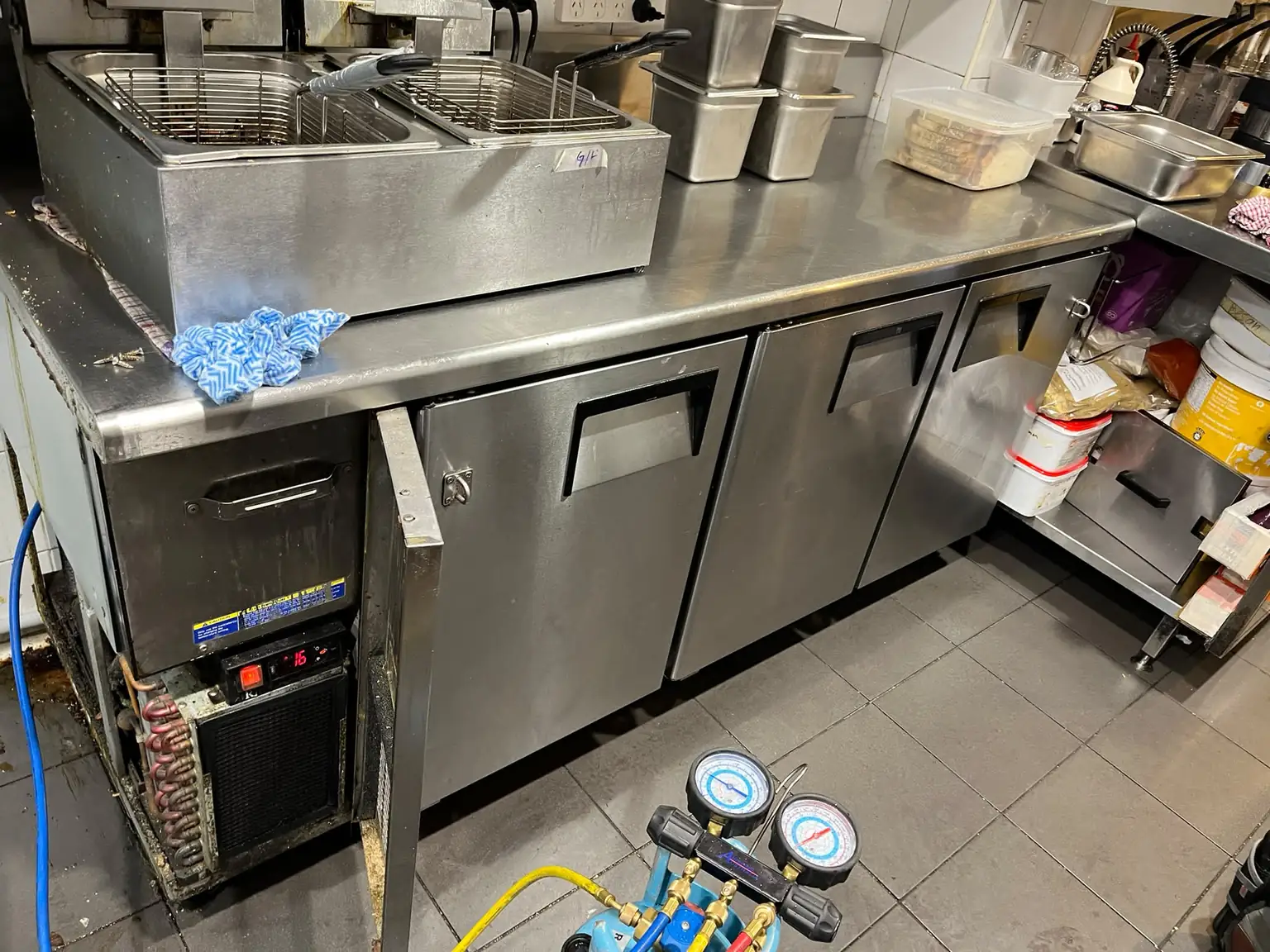 Self-contained under-bench kitchen fridge being repaired with refrigeration gauges connected